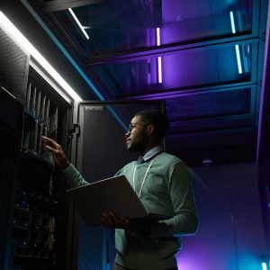 Mann mit Laptop steht vor einem Server